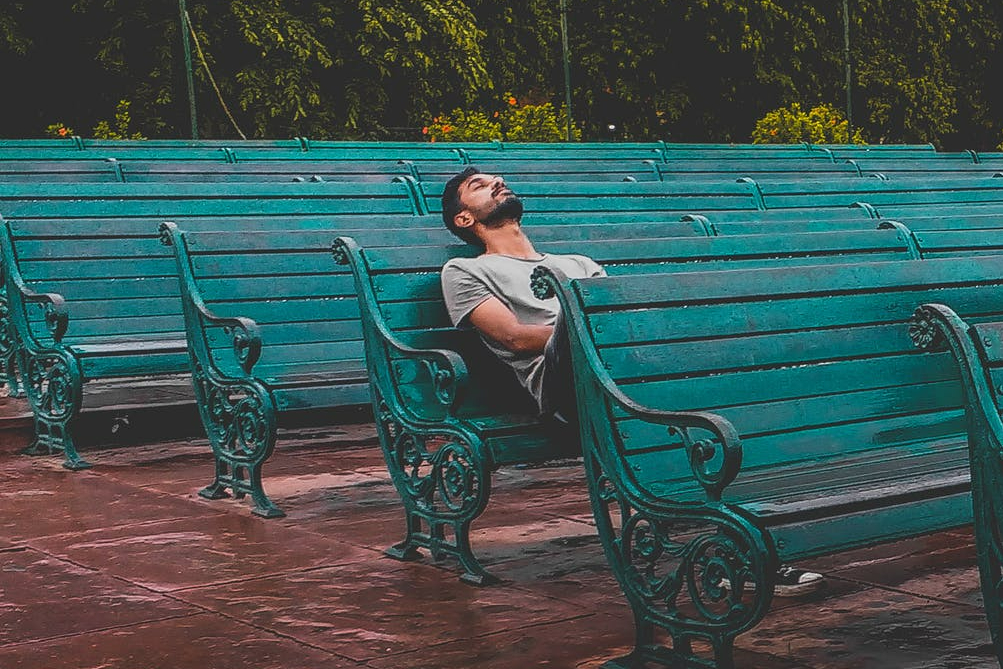 man sitting and closing eyes on teal bench